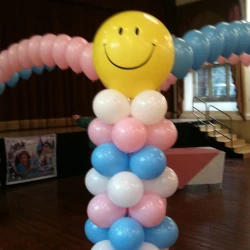 A balloon pillar topped with a yellow smiley face balloon