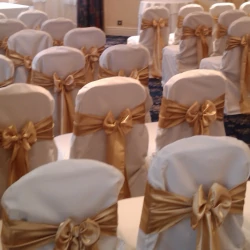 Chairs arranged in rows with white chair covers and gold satin sashes